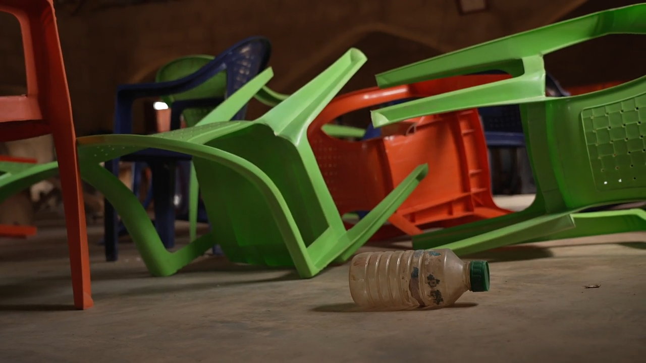 Green and orange plastic chairs lying on their side with a plastic bottle in the foreground, also on its side.