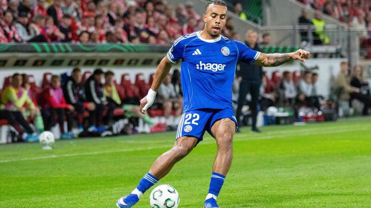 Guela Doue crosses the ball with his right foot, kicking from left to right across the screen. He is wearing Strasbourg's all Blue kit.