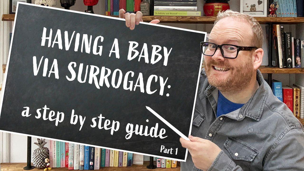 A smiling Kevin holds up a blackboard that reads: "Having a baby via surrogacy: a step by step guide". In the background is a bookshelf with lots of different coloured books. 