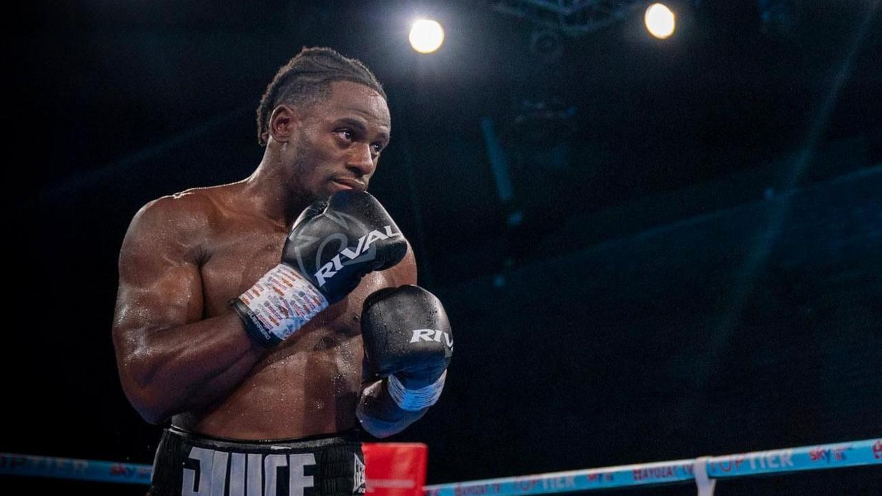 Gideon Onyenani is pictured in a boxing ring wearing black boxing gloves. Stage lighting can be seen high above him.