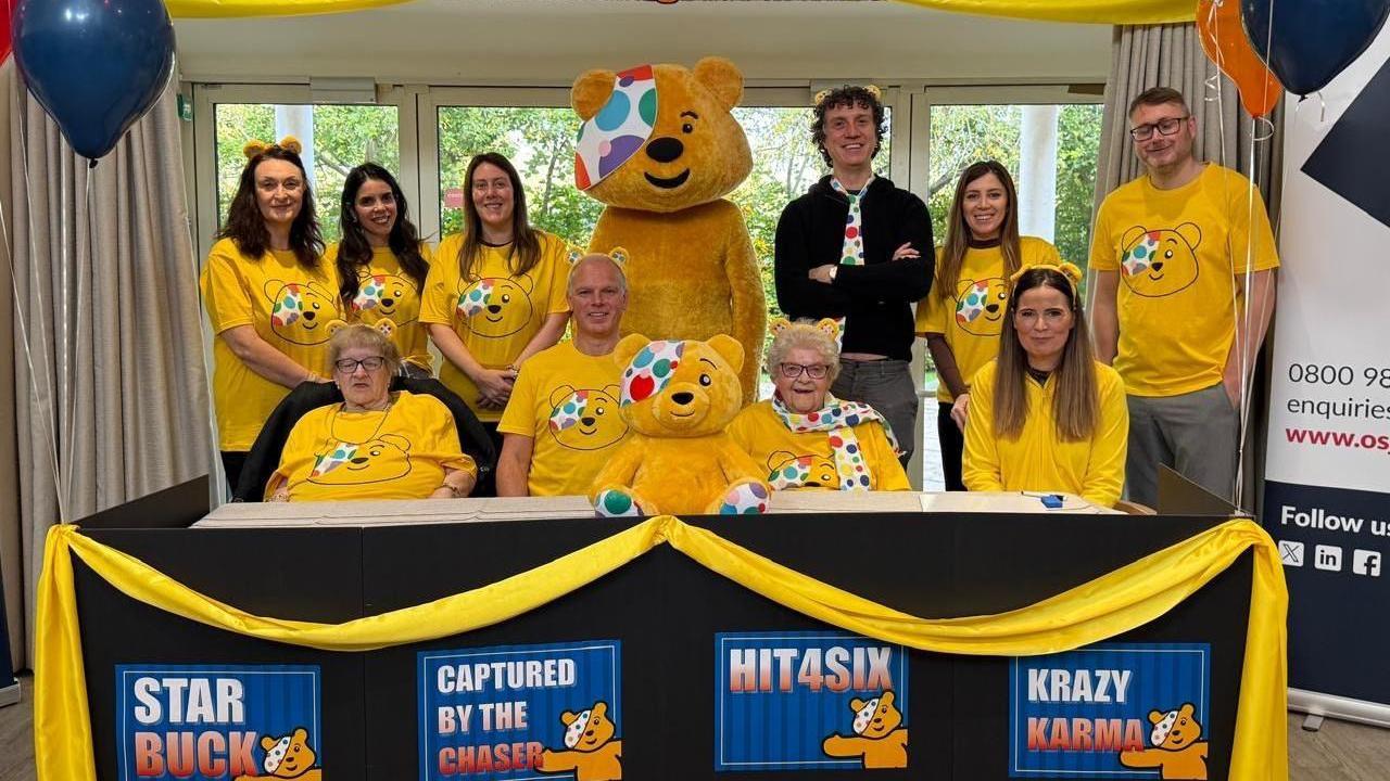 A team photo of care home residents and staff all wearing yellow, with Pudsey and Darragh Ennis