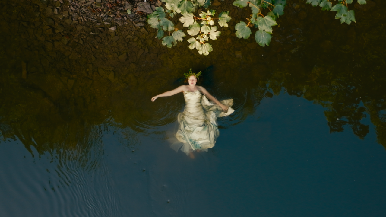 Megan Ruth-Trump is floating in the river. She is seen from above. She is wearing a dress.