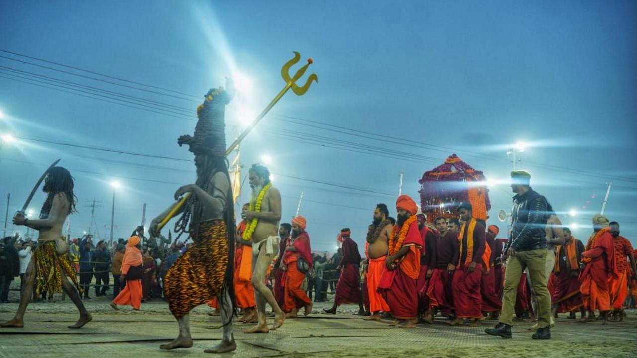 Holy men clad in saffron robes , wearing garlands of marigold, walk towards the river for the dip