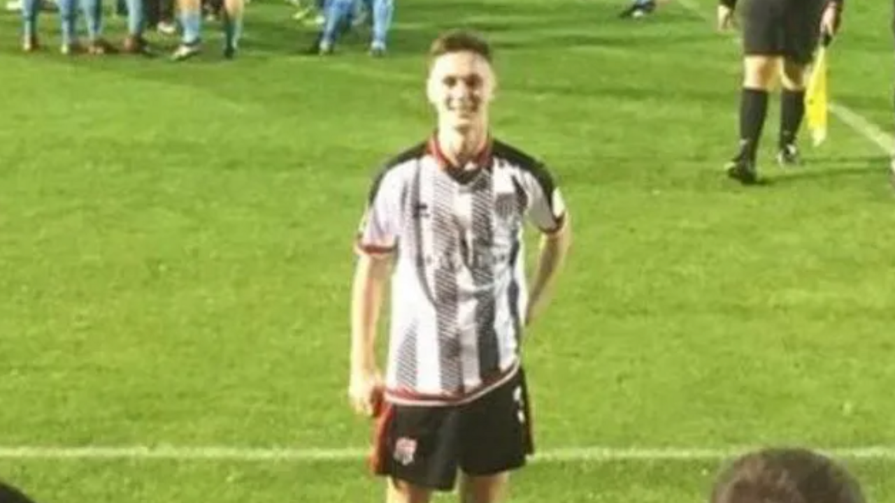 Ben Saunders on a football pitch. He is wearing black shorts and a striped shirt which has thick vertical white and grey stripes