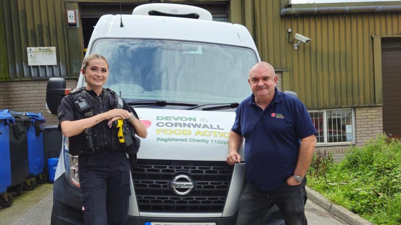 A photo which shows a female police officer stood next to a Devon and Cornwall Food Action van and a man from the charity on the right. 