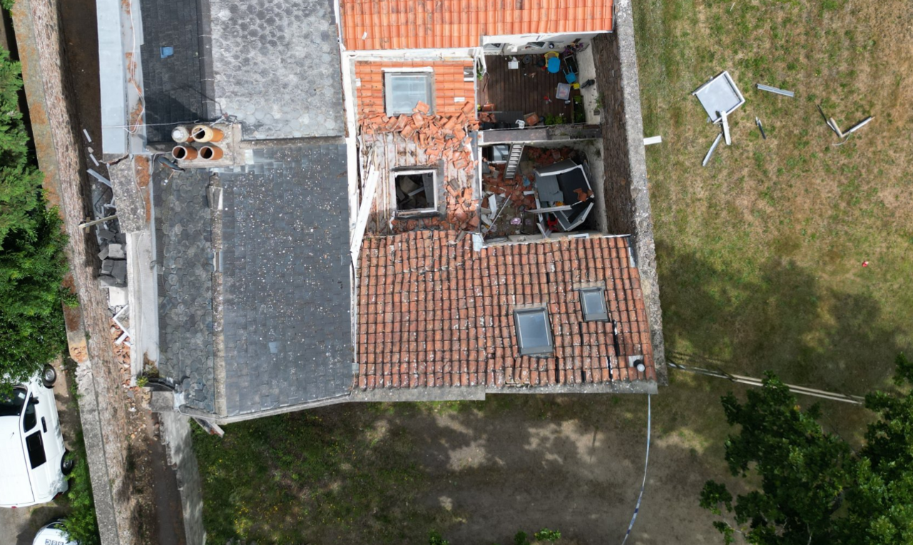 Aerial view of the damaged house with broken tiles on the roof and debris in the garden