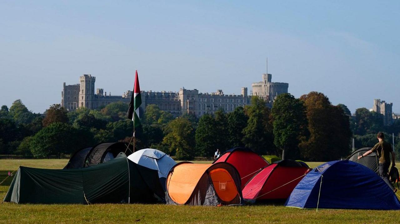 A group of about eight small tents in a park with Windsor Castle in the distance