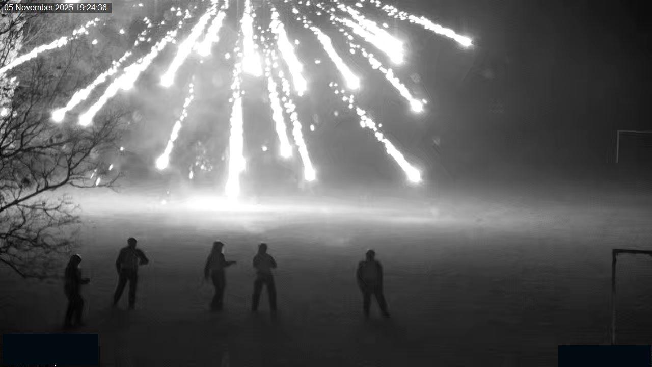 Black and white CCTV footage of five police officers with exploded fireworks raining down in front of them