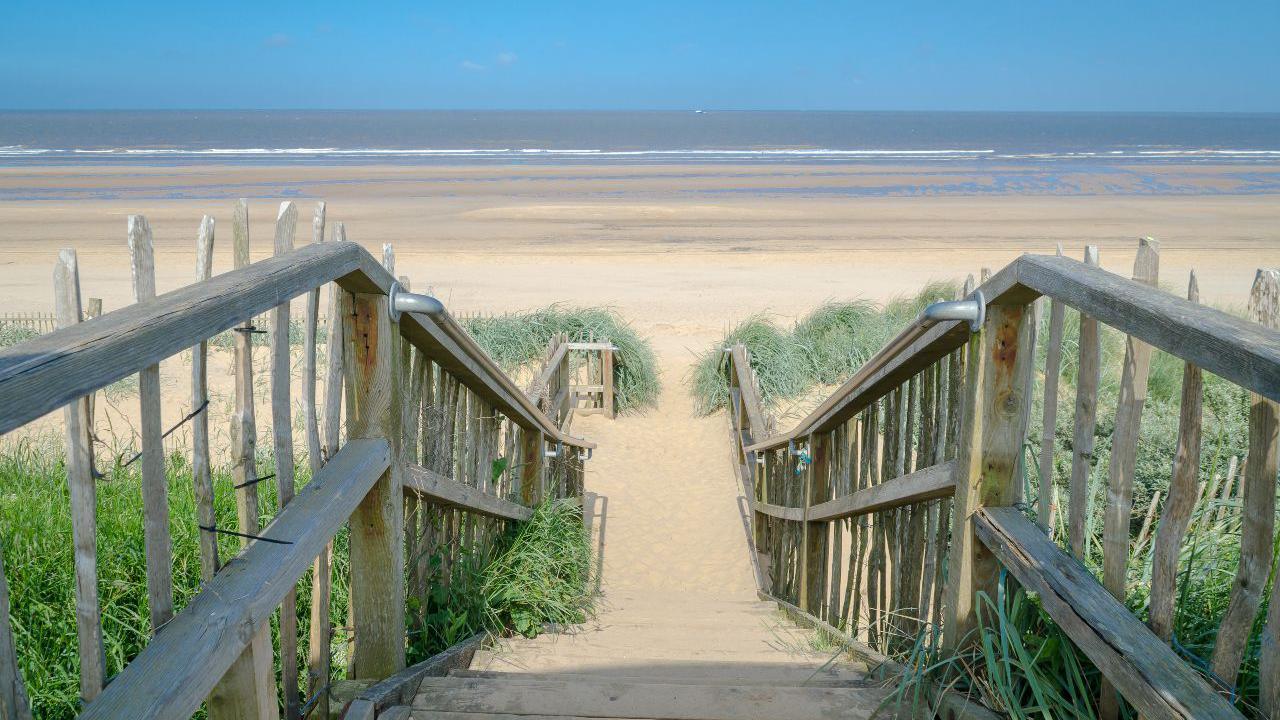 Wooden steps leading to a golden sand beach, with the sea in the distance