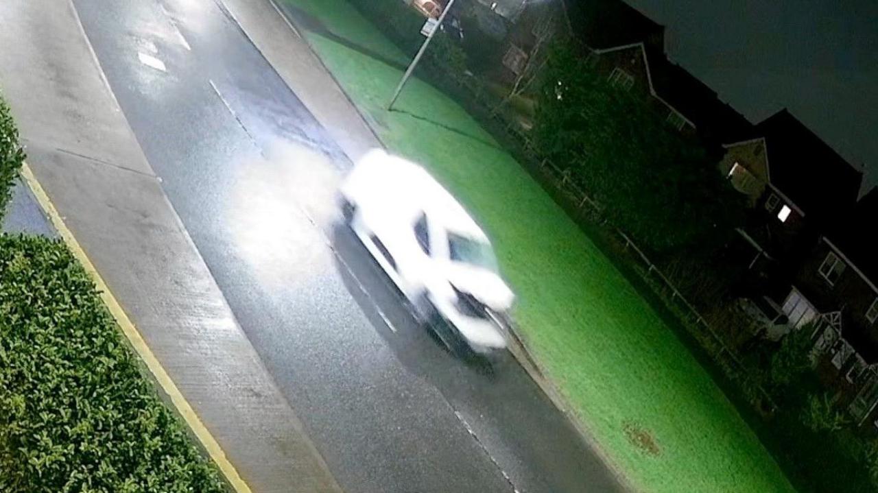 A CCTV still of a blurry white van with a crumpled bonnet and smashed windscreen.