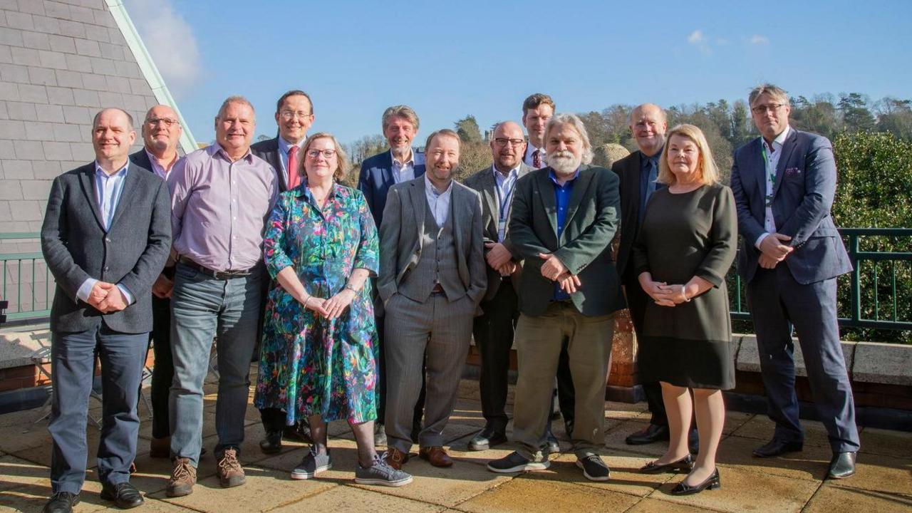 A 'team,' photo of 13 council leaders posing on a terrace with trees in the background
