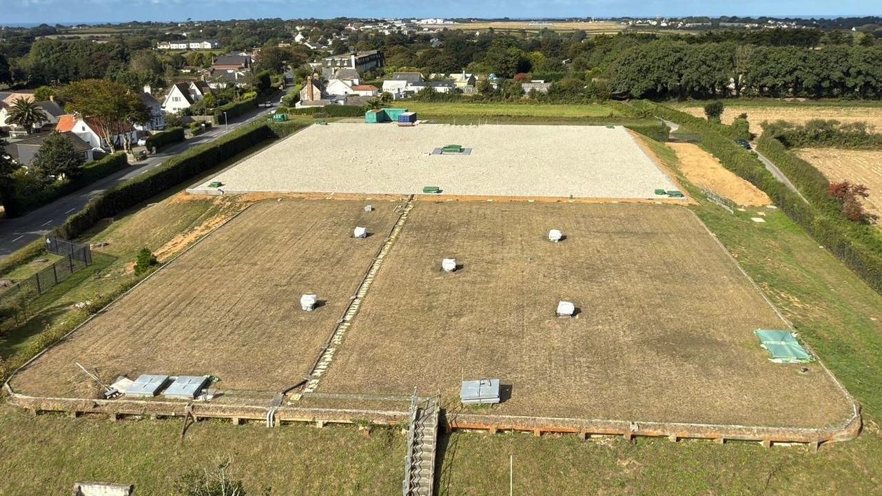 Drone shot of Guernsey Water's treated water service reservoir in Forest Road. The reservoir is in a rural area with lots of trees and fields surrounding it. Several houses and other buildings are nearby.