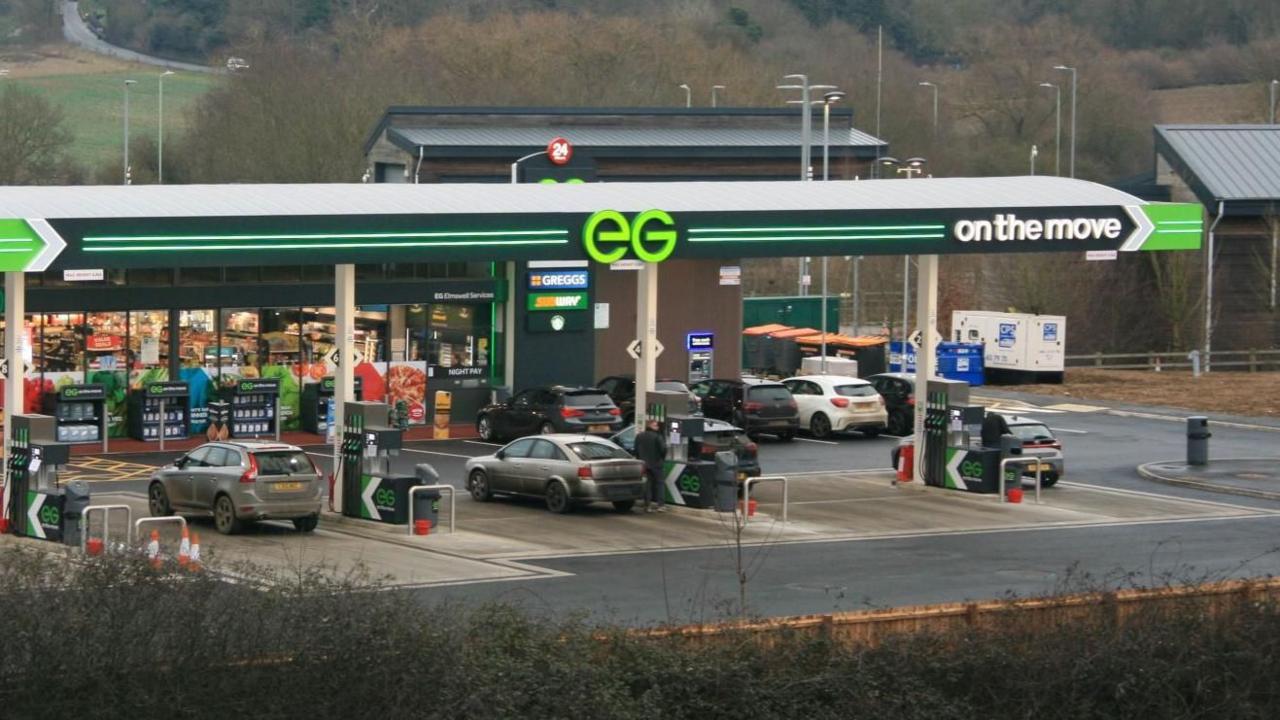 A filling station forecourt seen from a wide angle, with cars at pumps, a shop beyond and "EG On the Move" written across the forecourt roof