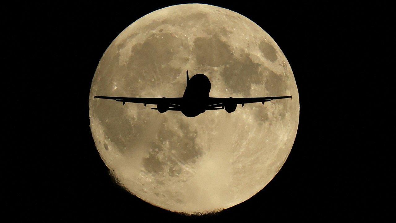 silhouette of a passenger plane as it passes in front of a big grey supermoon