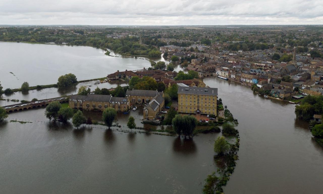 A bird's eye view of a river surrounded by flood water with houses in the middle