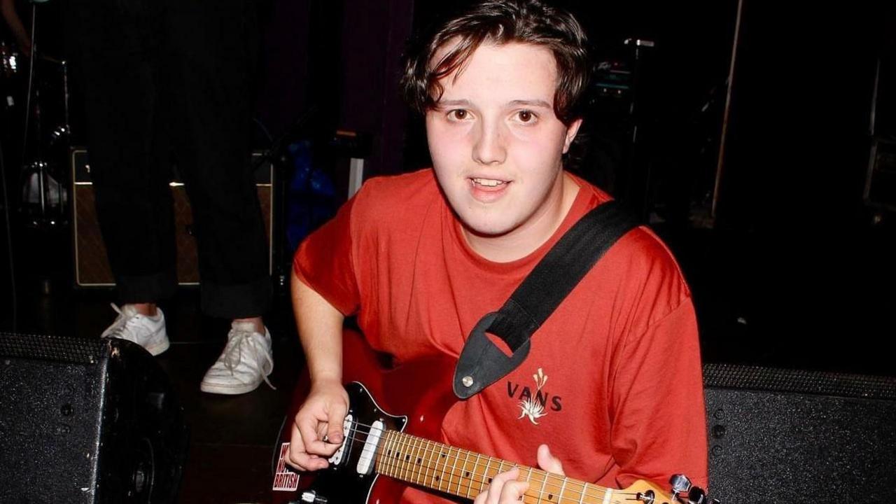 Gwydion Outram, wearing a red T-shirt, playing guitar 