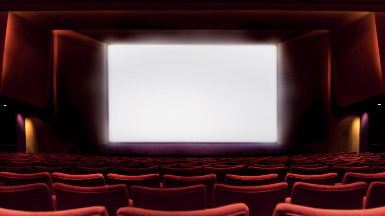 A blank cinema screen with rows of red chairs in the foreground