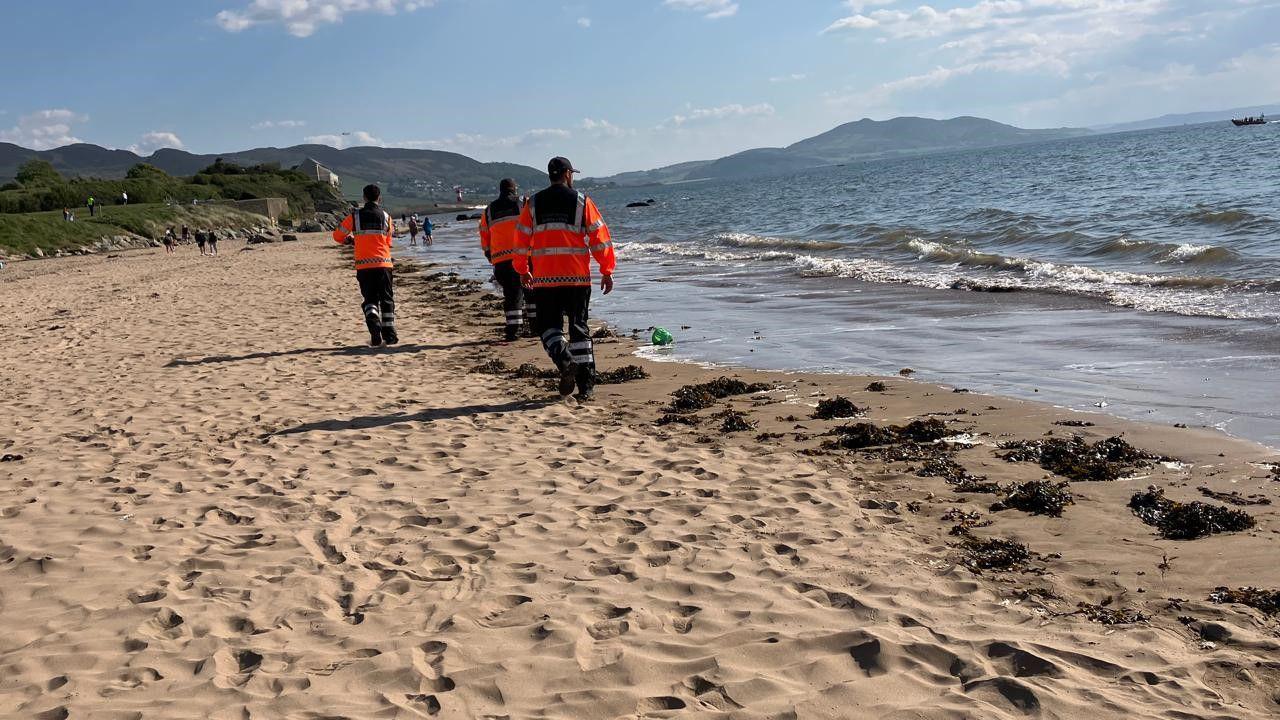 Three people in high viz walking along a shoreline.