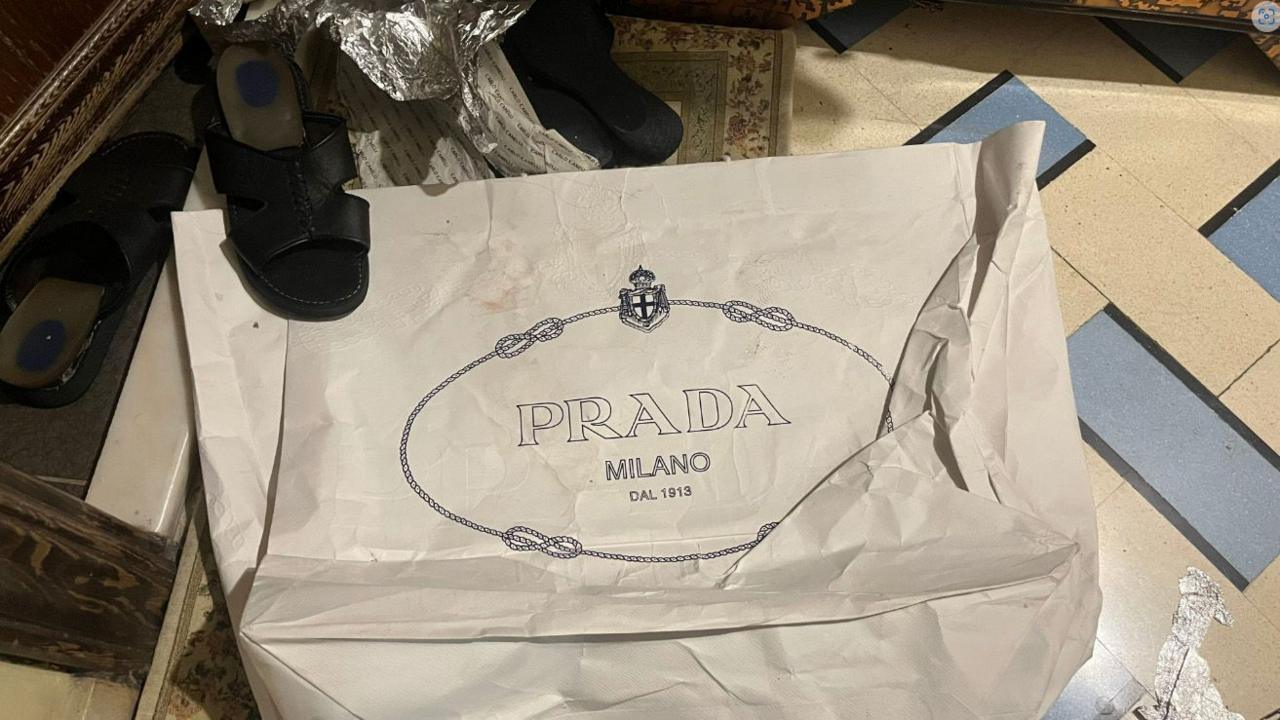 A white carrier bag with the words Prada Milano on it, with a sandal on top of one corner of the bag