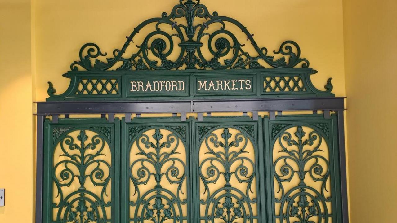 Decorative iron panels with scrollwork and the words Bradford Markets in gold against a yellow wall