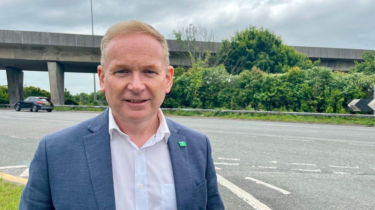John Stephens, the cabinet member for transport, in a white shirt and blue blazer with a green Plymouth City Council badge