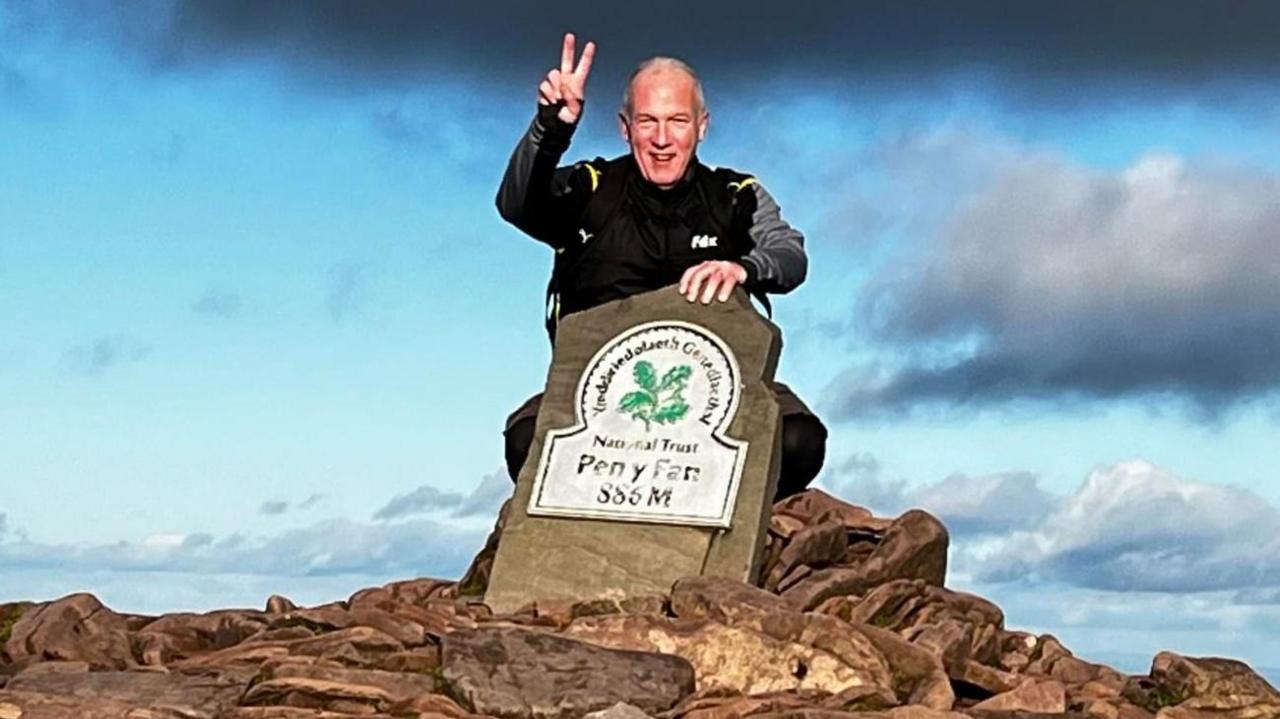 A man at the top of Wales' highest peak, Pen y Fan, makes a peace sign with his fingers