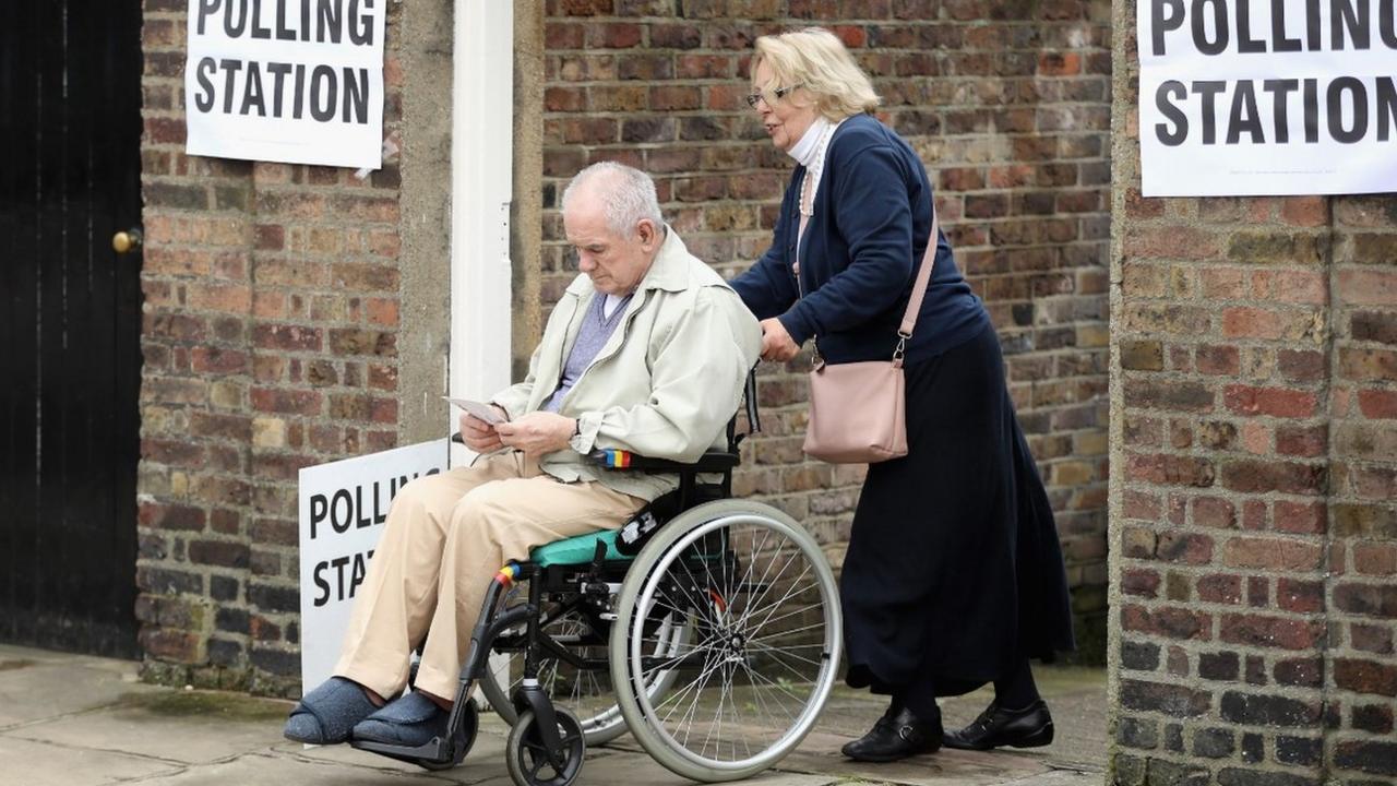 Woman pushing a man in a wheelchair out of a polling station