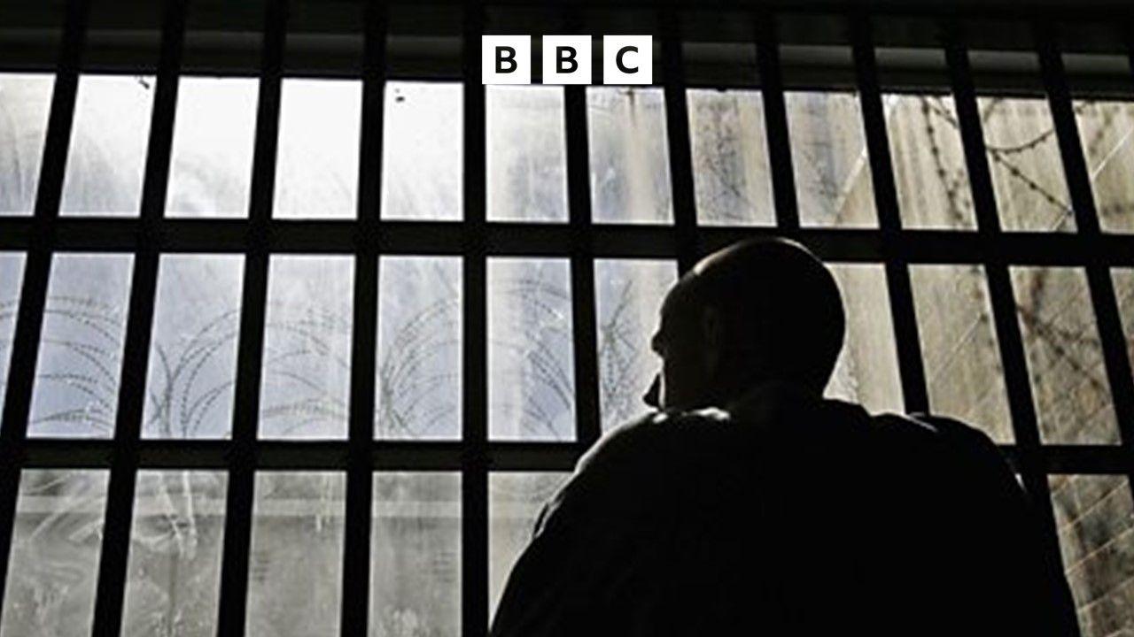 A silhouette of a man looking out of a dirty window. The window is made up of lots of rectangles.