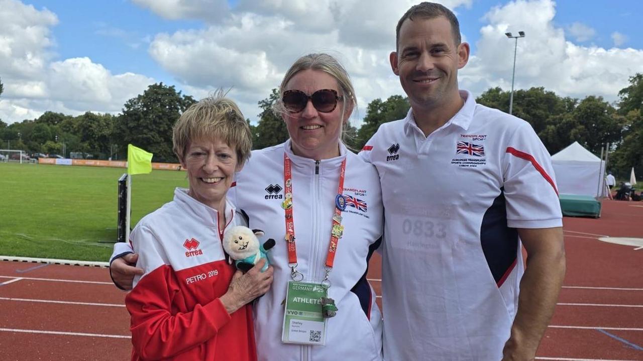 Three athletes posing for a team photo on a running track outdoors