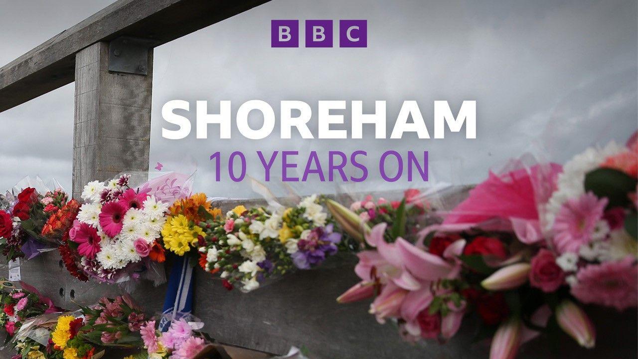 Bunches of flowers are placed in remembrance on a wooden bridge. 
The words 'Shoreham 10 years on' are written on the image in white and purple font.