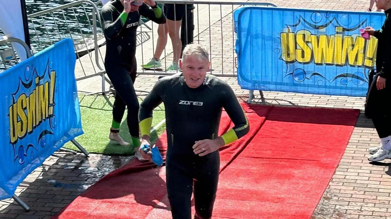 Tony Pilkington runs along a red mat after the swim section of a triathlete. 