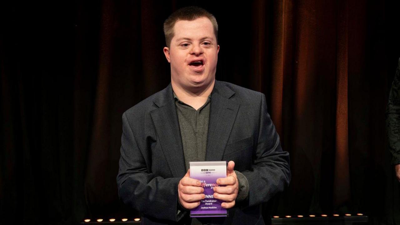 A man with a grey jacket and short hair is holding his award.