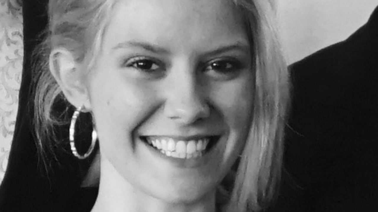This is a black and white close up photo of Chante. She is smiling at the camera with her blond hair up and a long piece of fringe falling to the right hand side of her face.