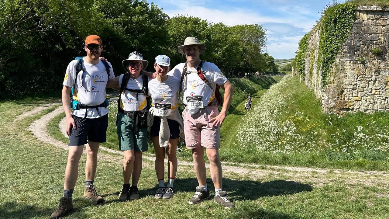 Debs Goodenough posing with her sons and daughter-in-law next to stone ruins surrounded by a grass moat.