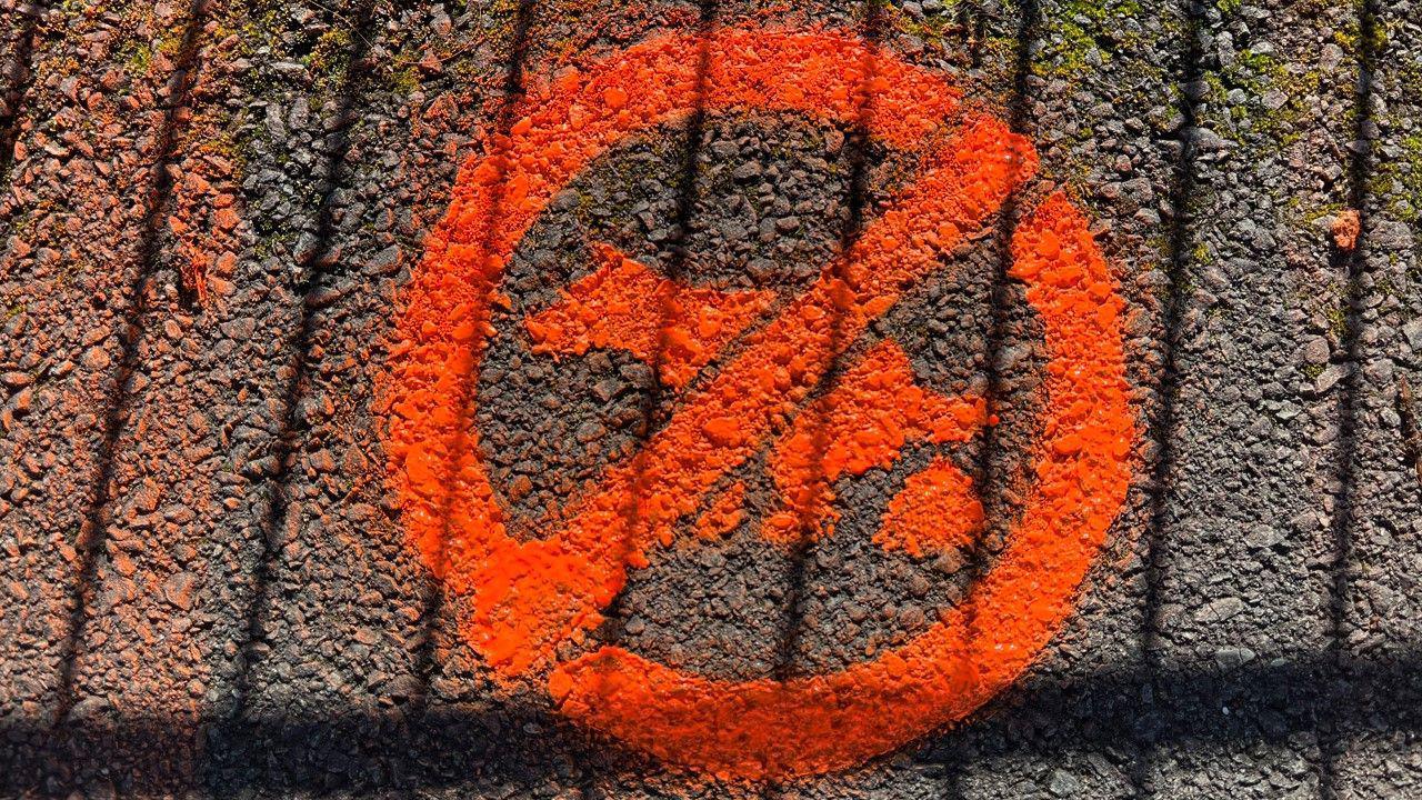 An orange paint sign stencilled on a pavement. It is in the format of a road sign - a circle with a dog defecating inside and a diagonal line through it.