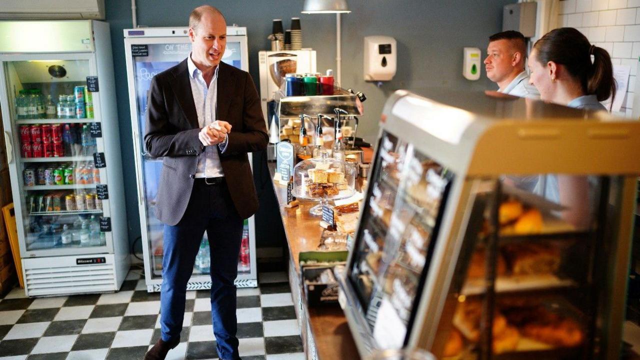 Prince William in a café talking to the people that run it 