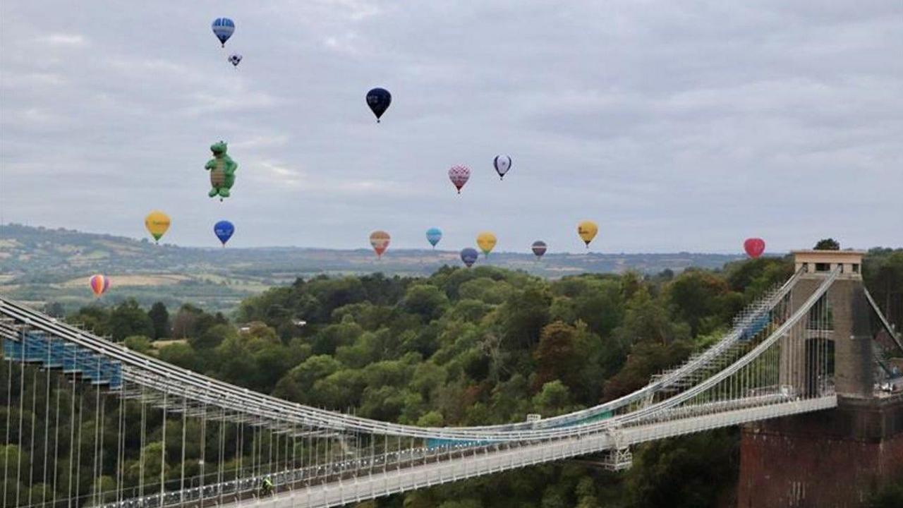Several colourful hot air balloons flying past the Clifton Suspension bridge on an overcast day
