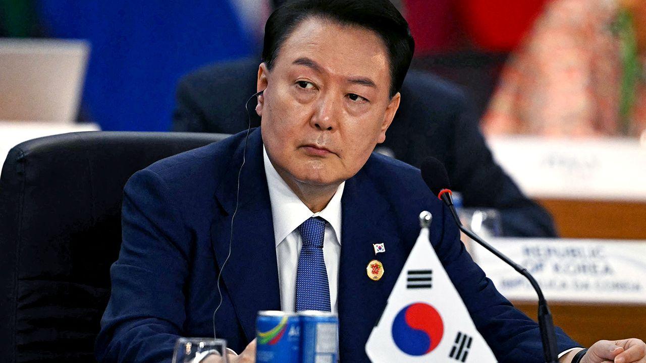 President Yoon Suk Yeol looks away from camera while wearing a suit and tie with an earpiece in, with a miniature South Korea flag and refreshments on the table in front of him as he sits during the third session of the G20 Leaders' Meeting in Rio de Janeiro, Brazil, on November 19, 2024.