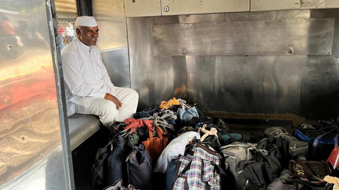 A man wearing a white kurta pajama and a cap sits in a train berth with lunchboxes placed on the floor