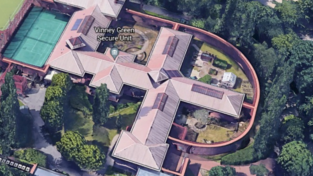 A bird's eye view of Vinney Green youth centre, which has an outdoor tennis court, several green lawns and is surrounded by trees. Its roofs are light red