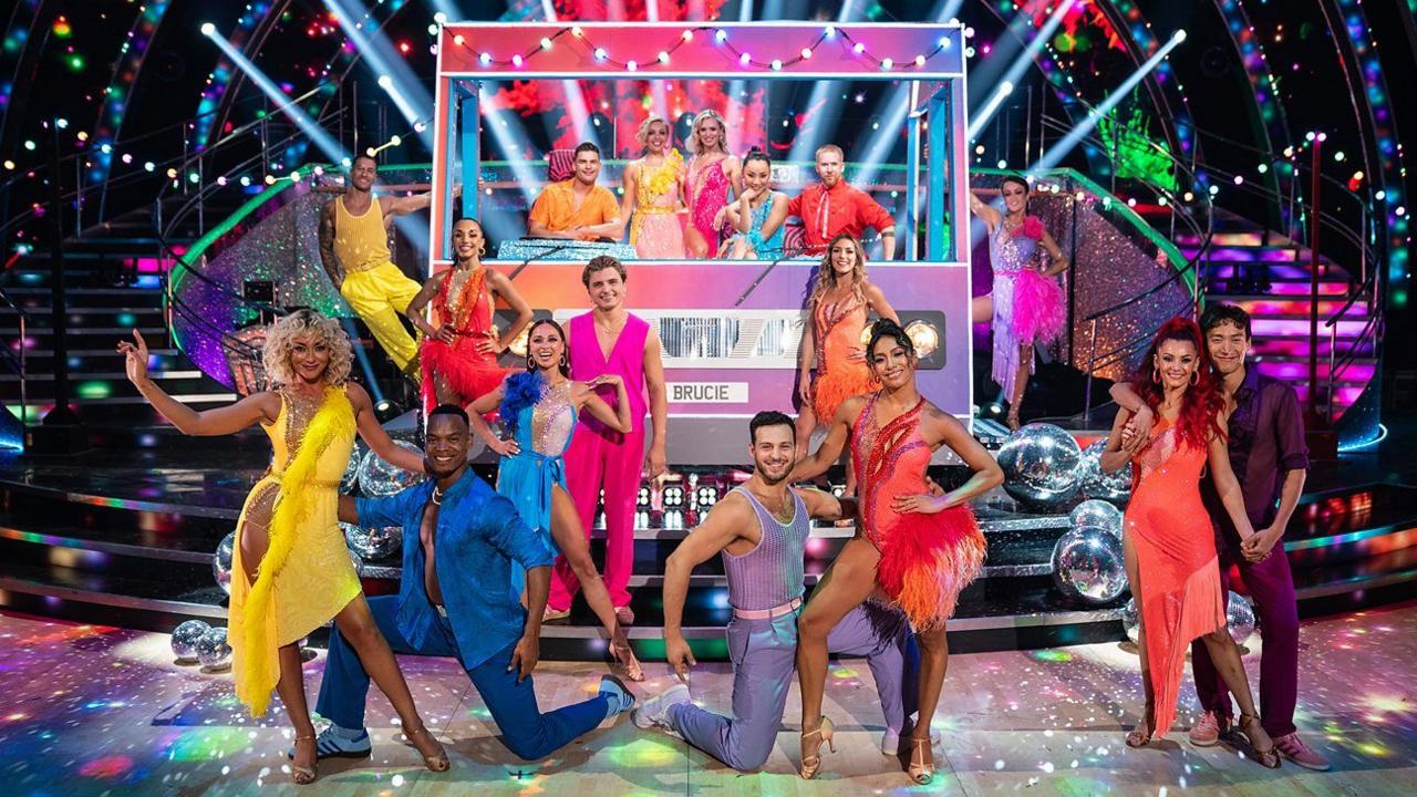 the professional dancers from Strictly pose by a cardboard bus in colourful dance outfits. 