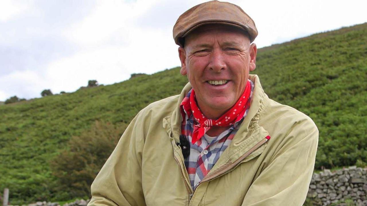 Llun o Gareth Wyn Jones, dyn yn gwisgo het brown yn gwenu wrth sefyll o flaen mynydd 