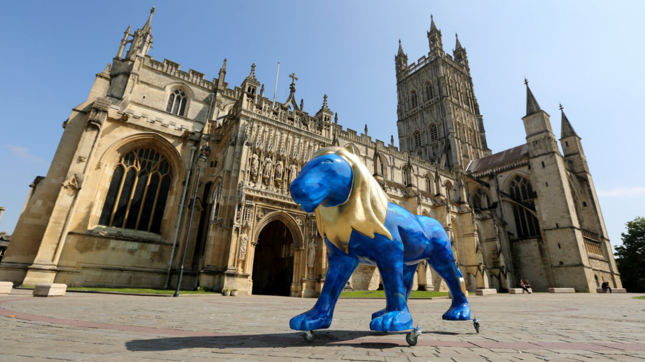 A blue and gold lion sculpture standing proudly outside Gloucester Cathedral.