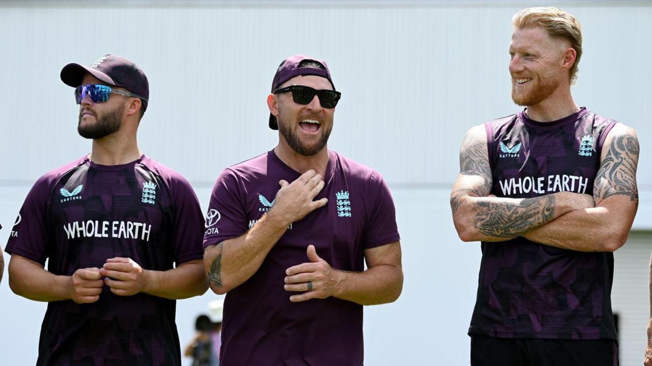 Three men in purple tops, caps and sunglasses smiling in the sunshine with one man showing heavily tattooed arms
