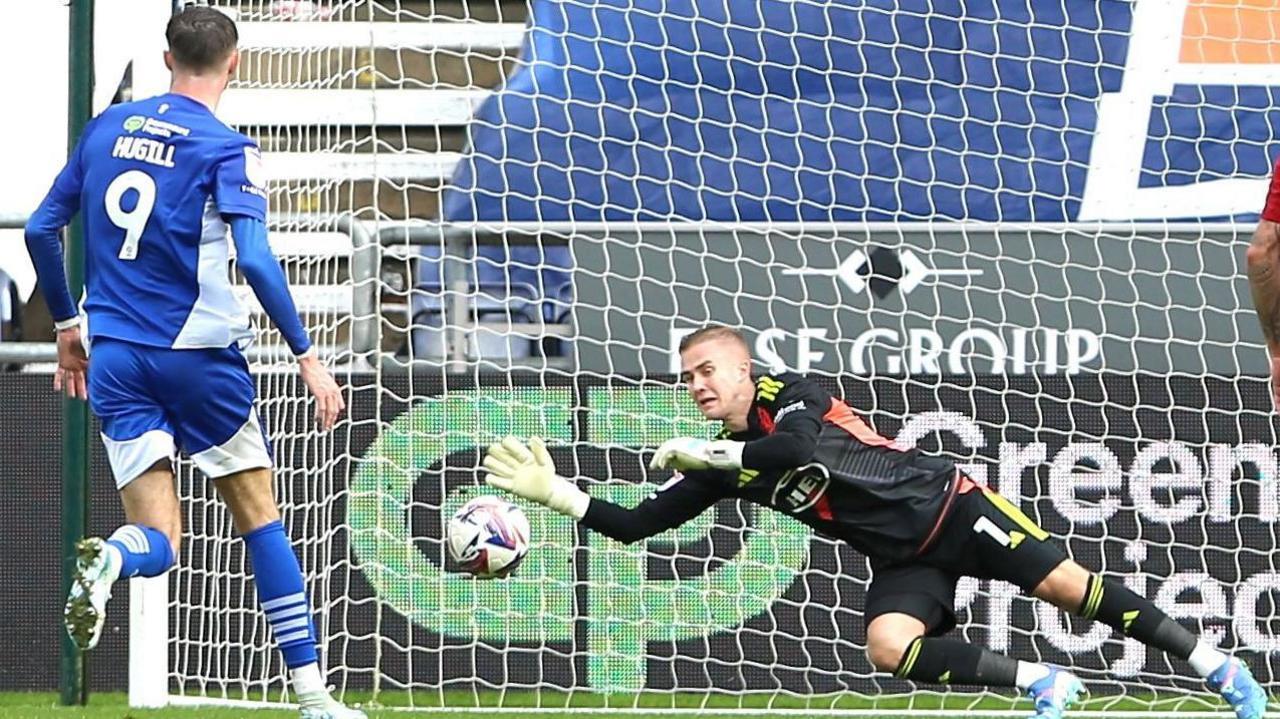 Exeter goalkeeper Joe Whitworth dives to his right to make a save against Wigan