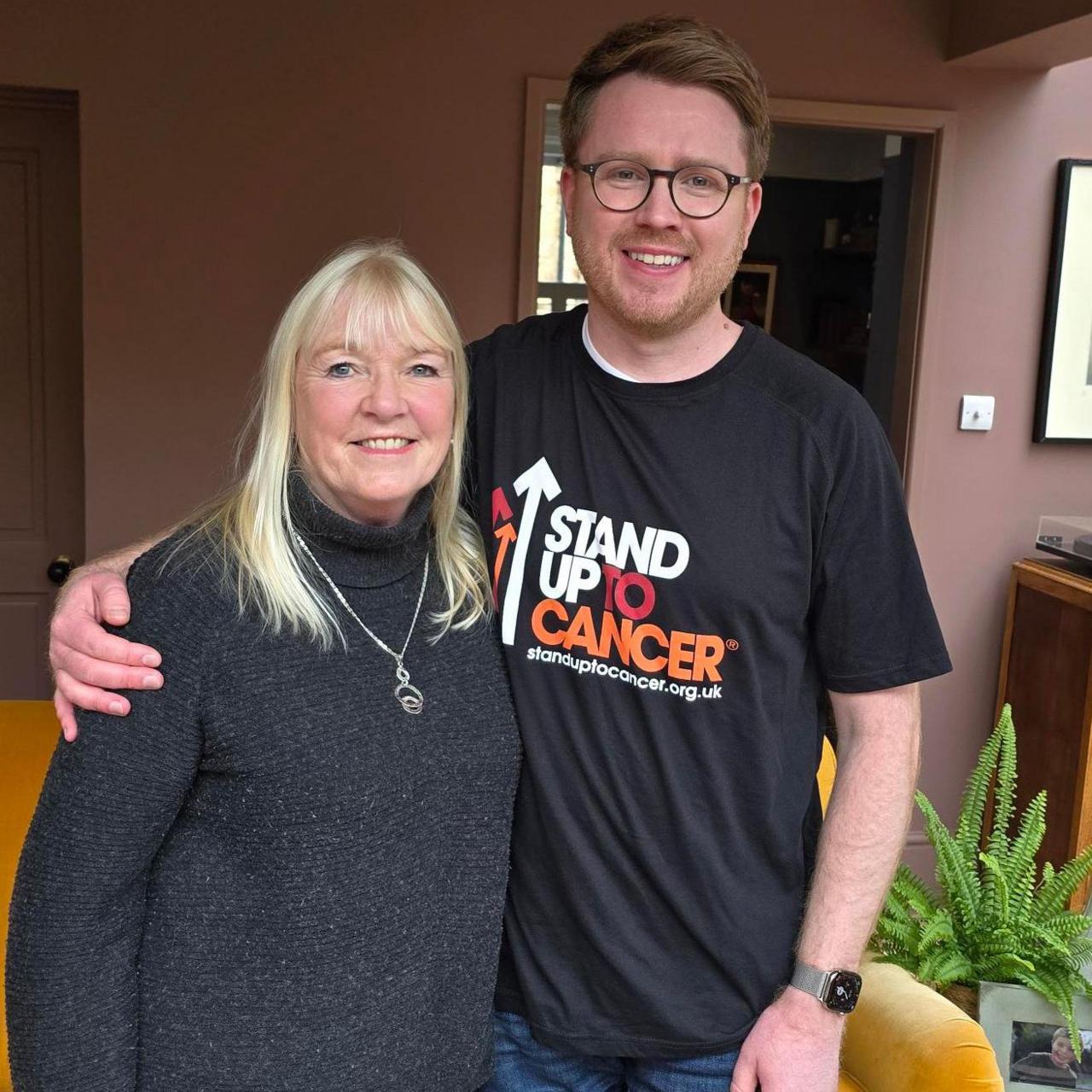 Jack wears his Stand Up To Cancer shirt and has an arm around his mum, who has long blonde hair and wears a thick grey polo neck.