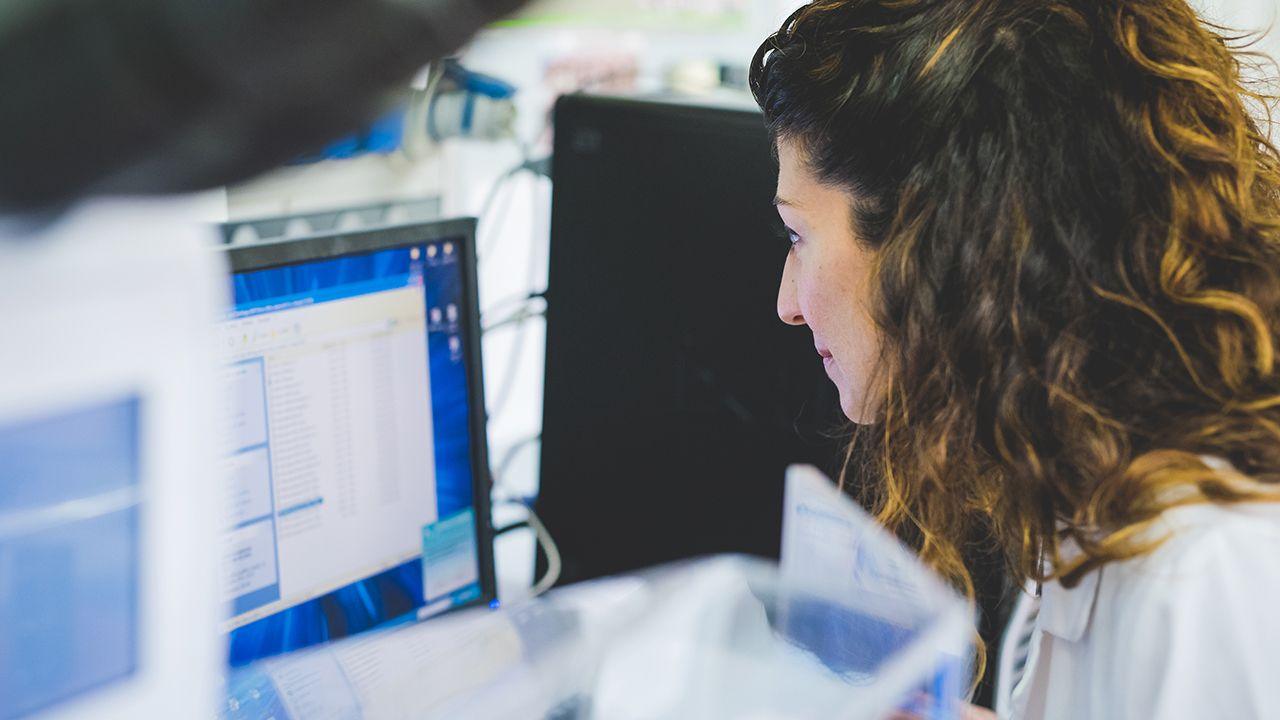 A woman looks at a computer screen in a lab setting, image is a generic stock photo and for illustrative purposes only.