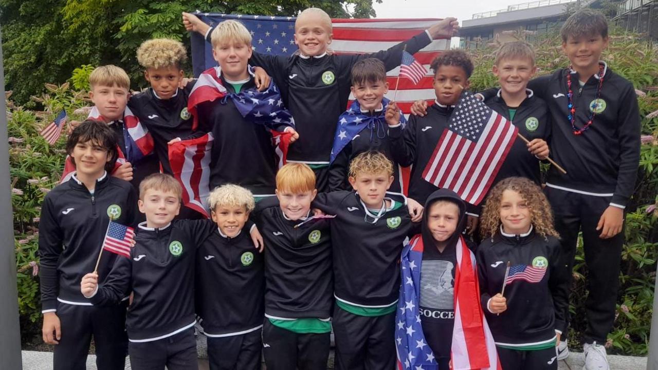 a group of young footballers pose in team colours. Some are holding US flags