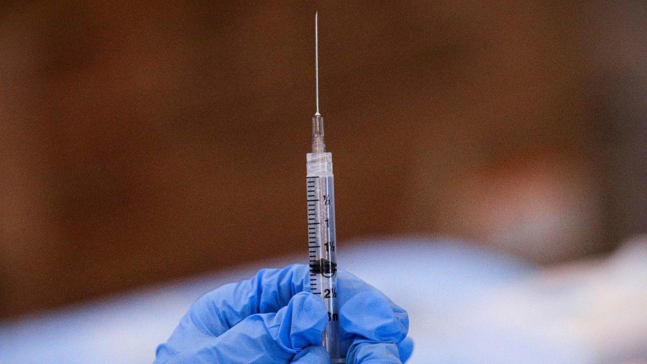 A syringe full of a clear substance with someone wearing blue gloves holding it up, against a blurred background.