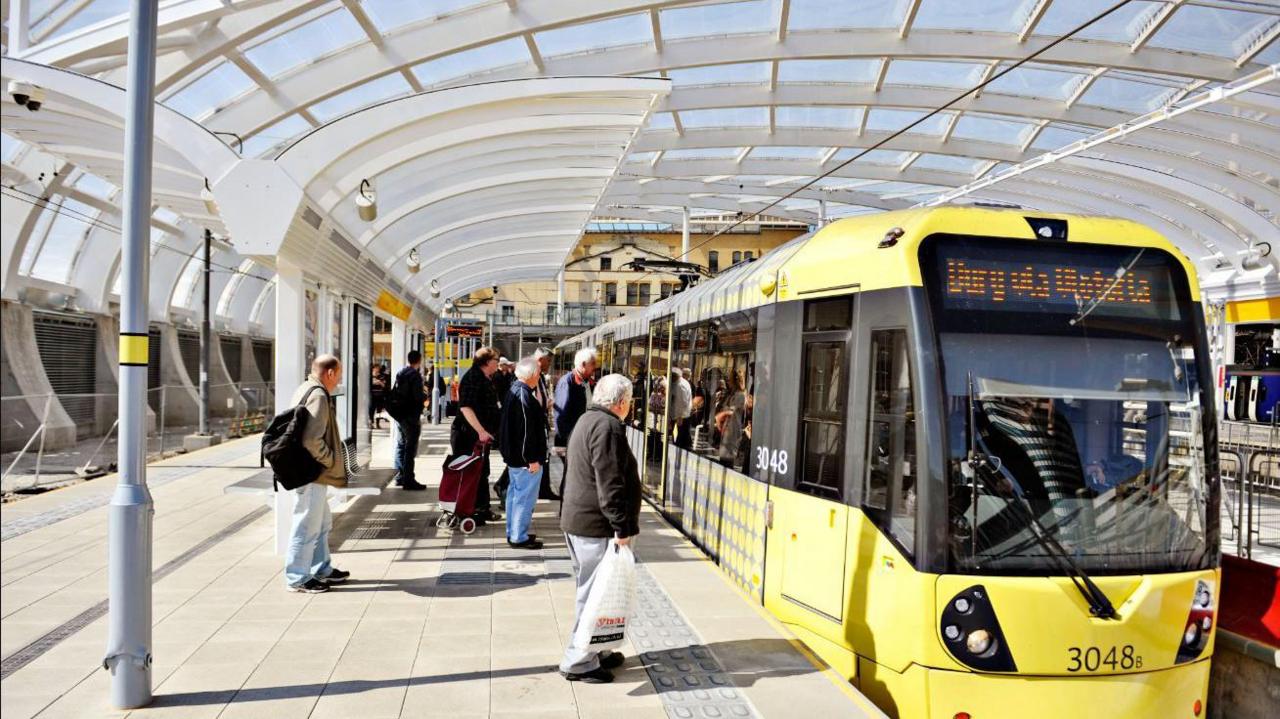 Passengers wait at a platform to get on a Bee Network yellow coloured tram.